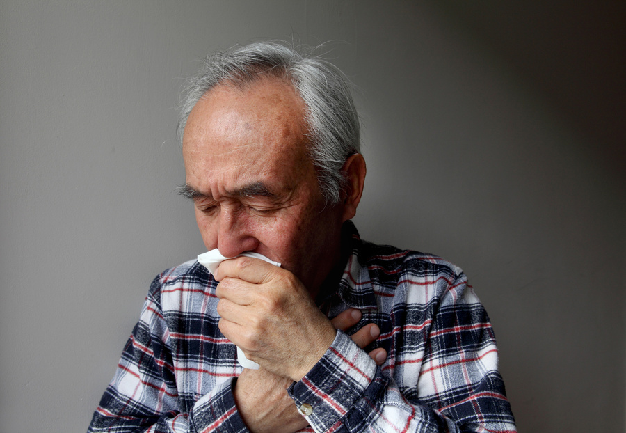 Older man coughing into napkin